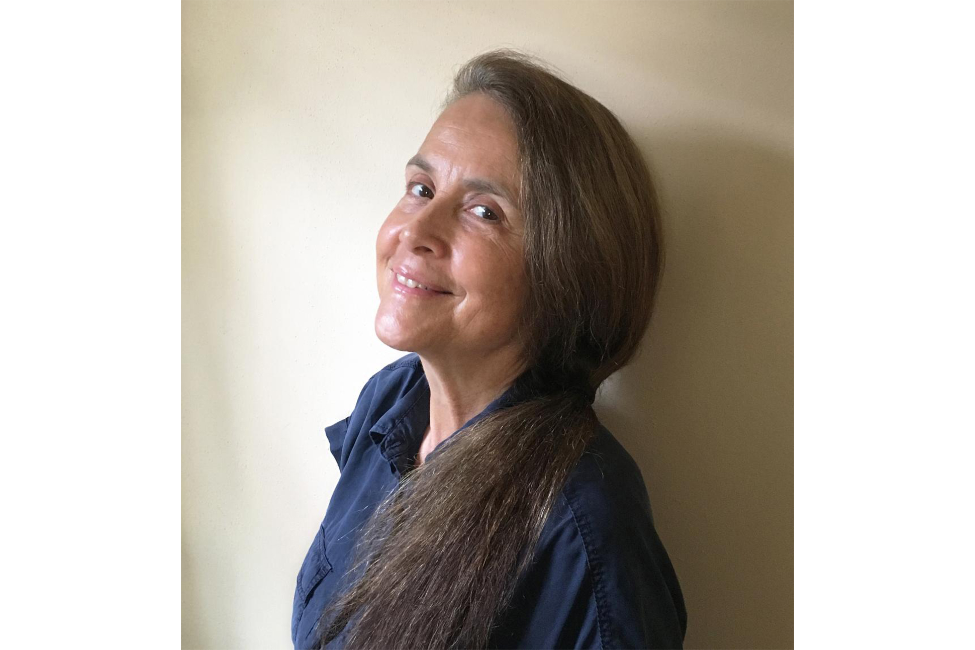 White woman with long hair in low ponytail smiling in front of a white wall
